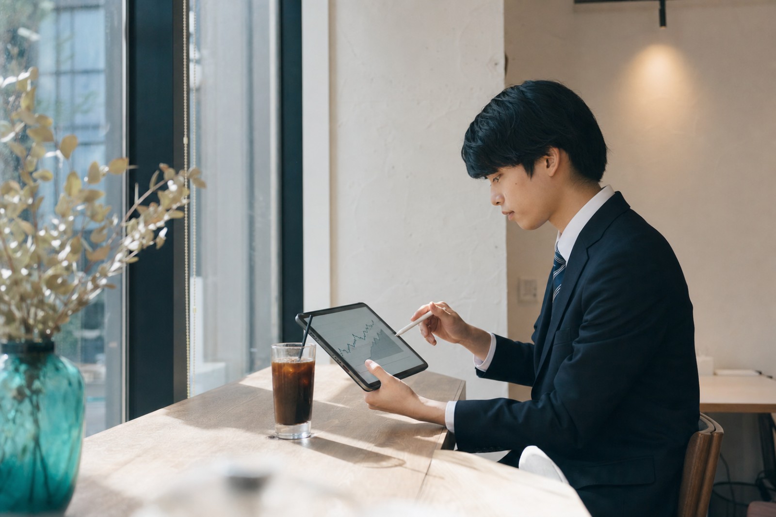 カフェでタブレットを使い外務員試験の学習に取り組むスーツ姿の20代